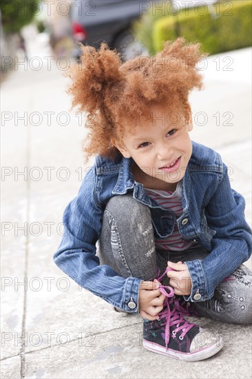 Girl tying sneaker shoelaces on sidewalk