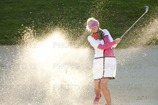 Caucasian woman hitting golf ball in sand trap while blindfolded