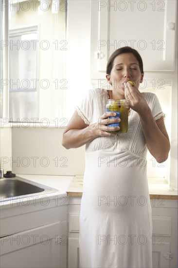 Pregnant woman eating pickles in kitchen