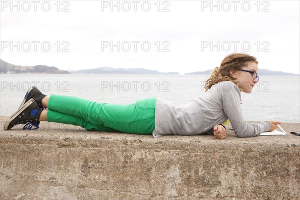 Caucasian girl laying on concrete wall over ocean