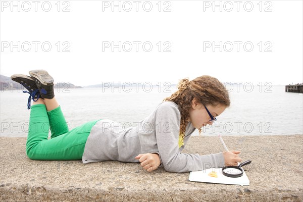Caucasian girl doing homework on concrete wall over ocean