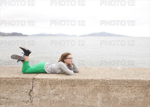 Caucasian girl laying on concrete wall over ocean