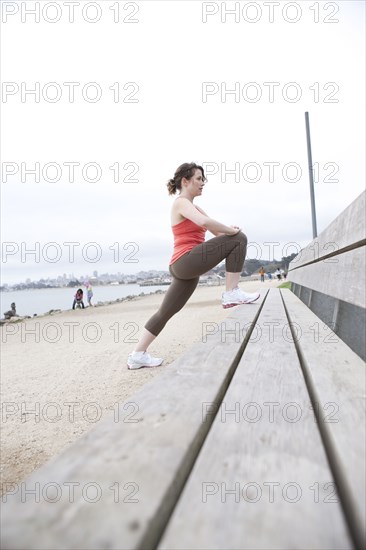Caucasian woman stretching on beach bench