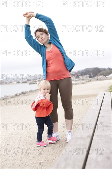 Caucasian mother and daughter stretching on beach
