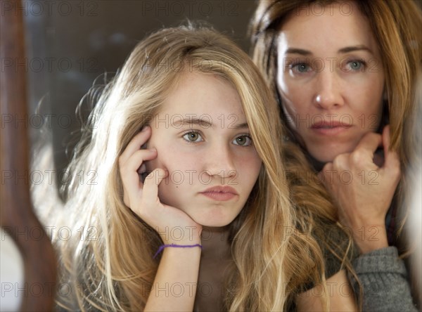 Serious mother and daughter examining themselves in mirror