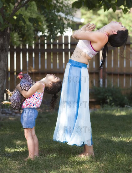 Mother and daughter practicing yoga with chicken in backyard