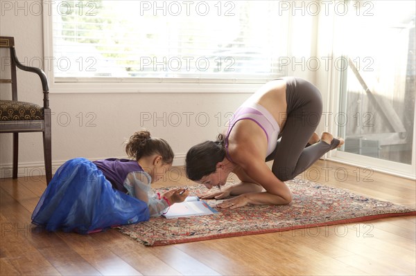 Woman practicing yoga and helping daughter with homework