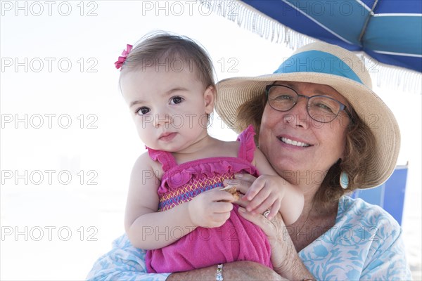 Caucasian grandmother and granddaughter sitting under umbrella