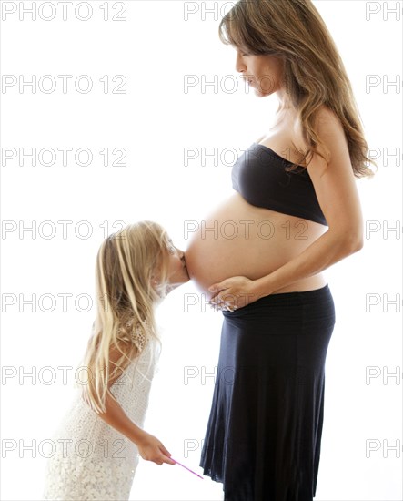 Caucasian girl kissing belly of pregnant mother