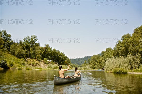 Rear view of women rowing canoe in rural lake