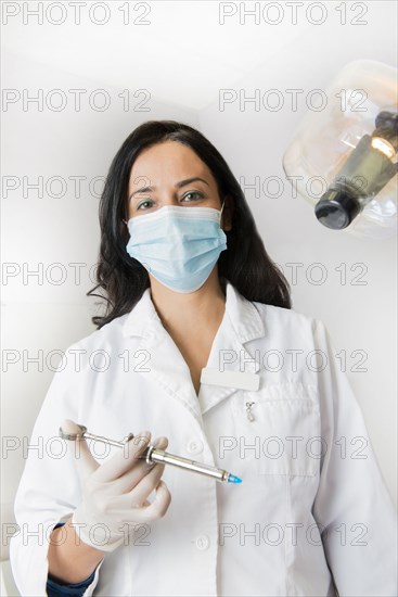 Indian dentist holding syringe by light