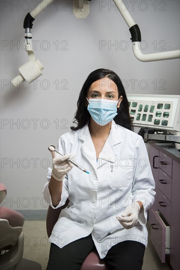 Indian dentist holding syringe in office