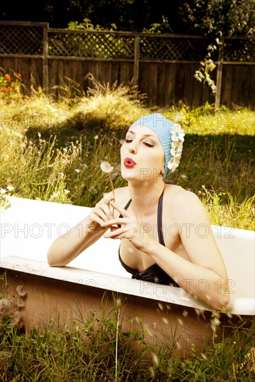 Woman wearing vintage swim cap in bathtub in backyard