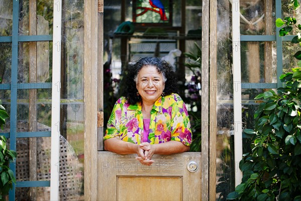 Hispanic woman smiling in garden greenhouse doorway