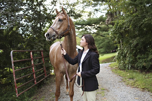 Equestrian woman walking horse on dirt path