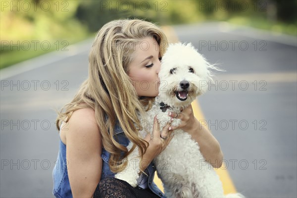 Close up of woman kissing dog on empty road