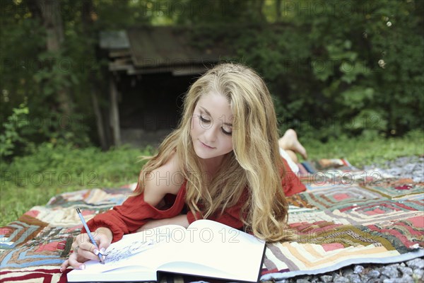 Teenage girl drawing in notebook on blanket