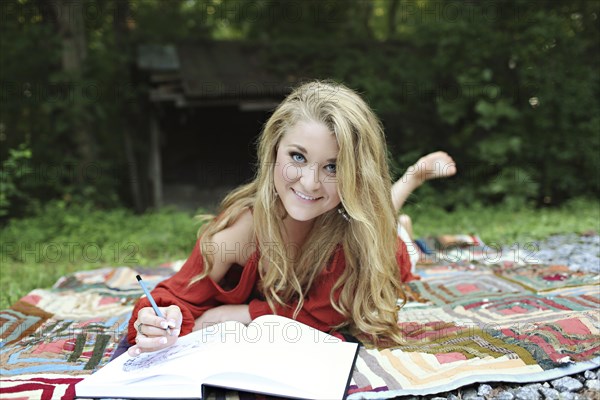 Teenage girl drawing in notebook on blanket