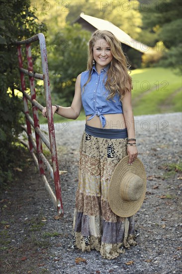 Teenage girl holding straw hat at rural gate