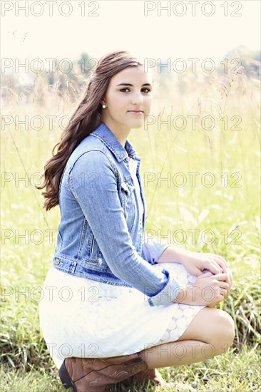 Woman crouching in tall grass in field