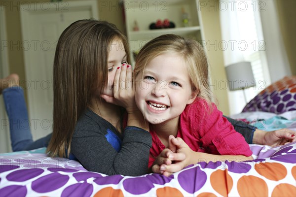 Close up of sisters whispering on bed