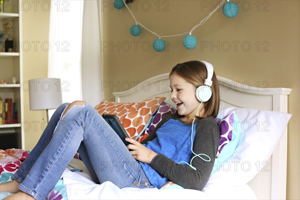 Girl listening to headphones with digital tablet on bed