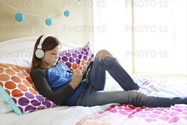 Girl listening to headphones with digital tablet on bed