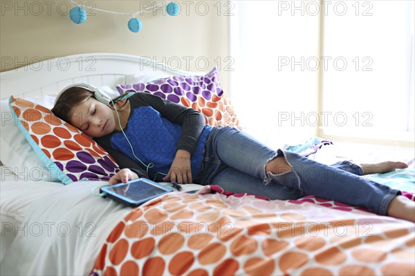 Girl listening to headphones with digital tablet on bed