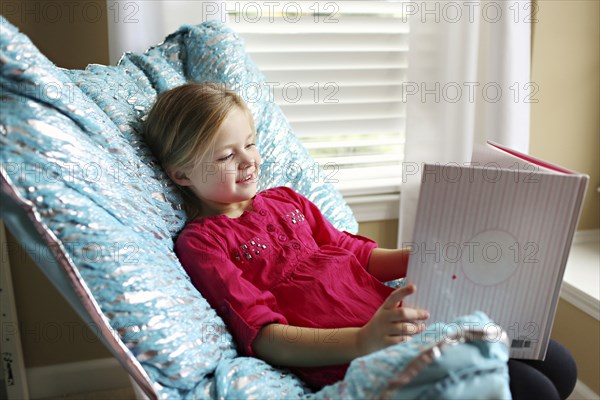 Smiling girl reading book in armchair