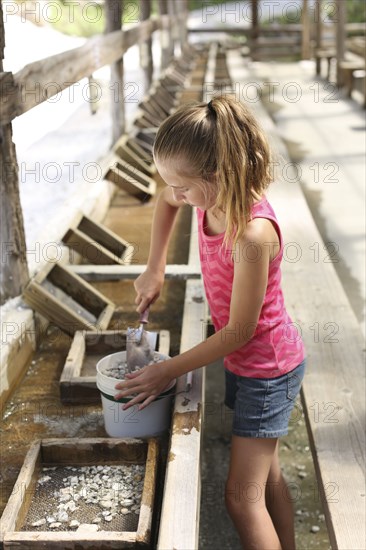 Girl shoveling rocks in bucket in trough