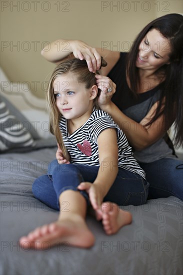 Mother styling hair of daughter on bed