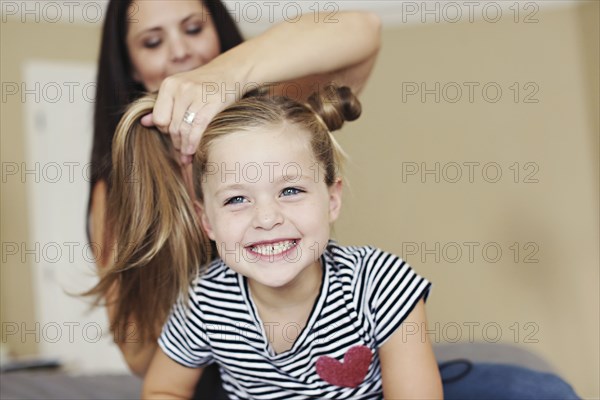 Mother styling hair of daughter on bed