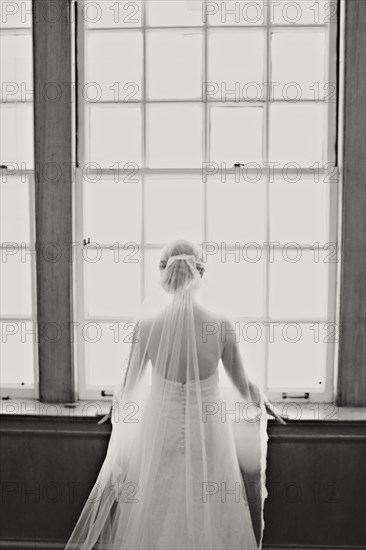 Bride in veil and wedding gown standing at window
