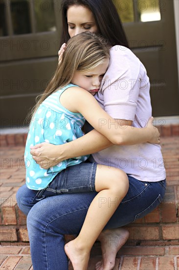 Close up of mother comforting daughter on front stoop