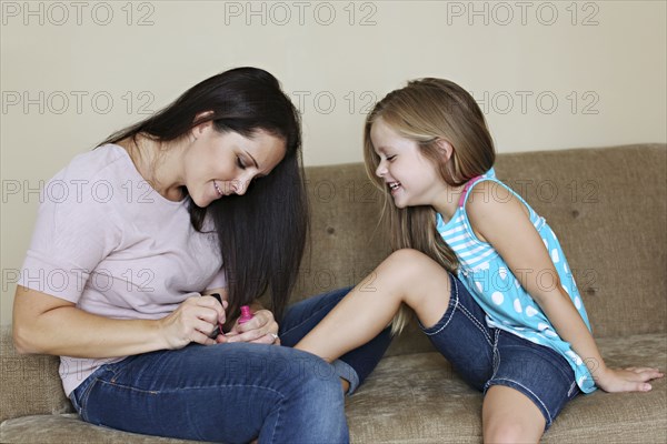 Mother painting toenails of daughter on sofa