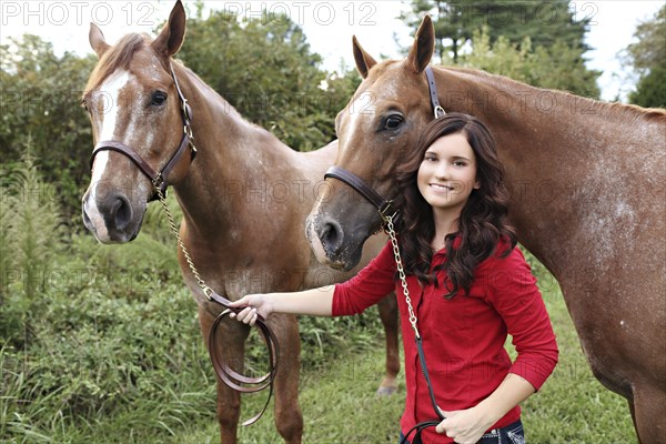 Teenage girl walking horses in rural field