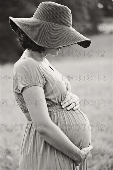 Pregnant Caucasian woman holding belly in field