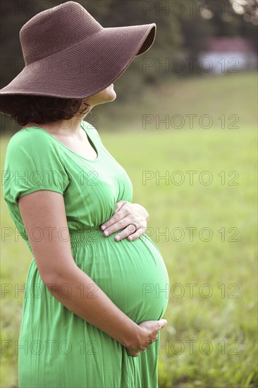 Pregnant Caucasian woman holding belly in field