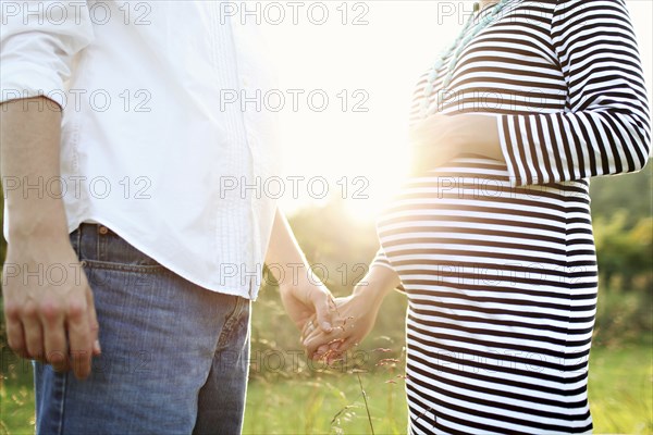 Pregnant Caucasian couple holding hands in field