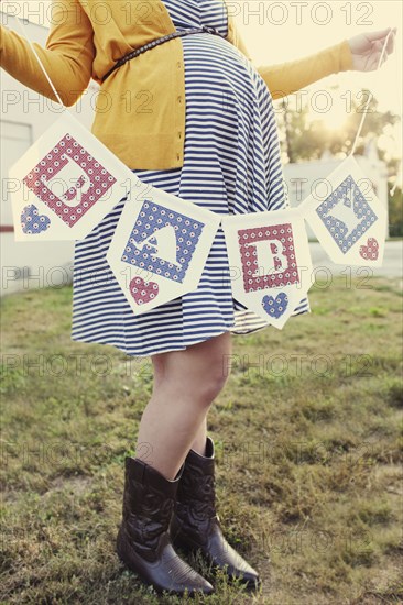 Pregnant Caucasian woman holding baby banner in backyard