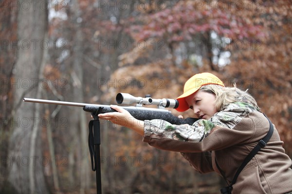 Hunter in camouflage aiming rifle in forest