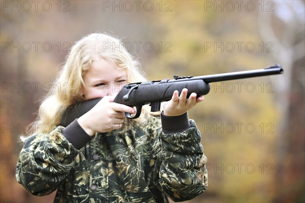 Girl in camouflage aiming rifle in forest