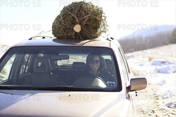Woman driving Christmas tree home on car roof