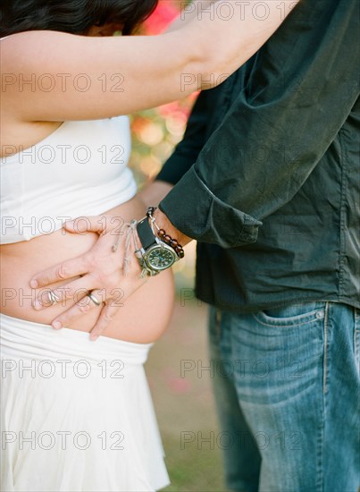 Man holding belly of pregnant wife in backyard