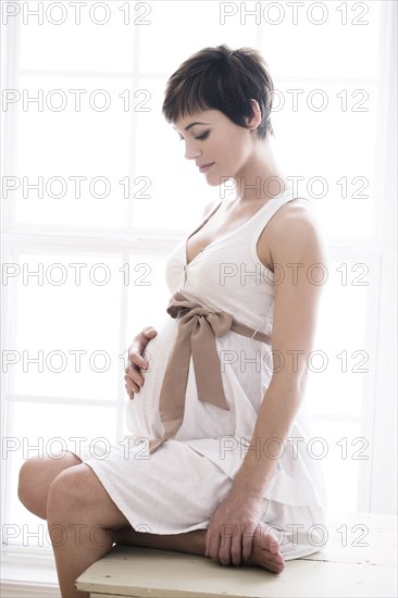 Pregnant woman holding her belly near window