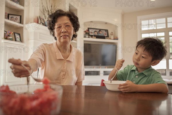 Asian grandmother feeding grandson at table