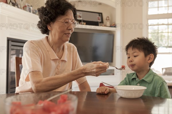 Asian grandmother feeding grandson at table