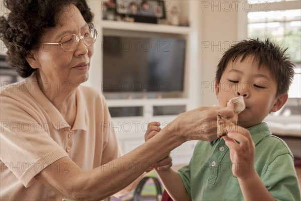 Asian grandmother wiping face of grandson at table
