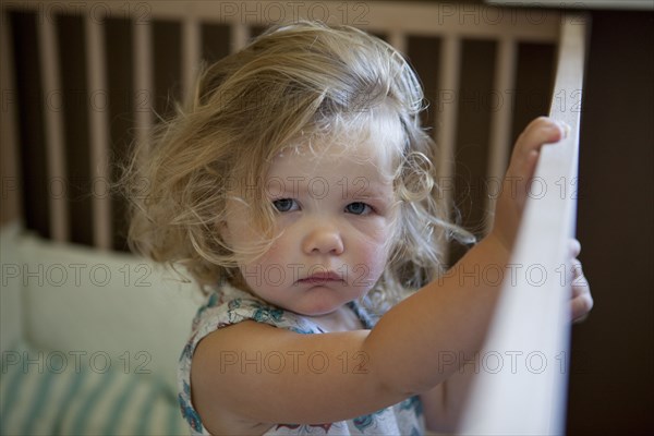 Pouting preschooler girl standing in crib