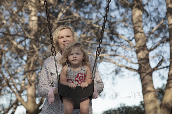 Grandmother pushing granddaughter on swing at playground